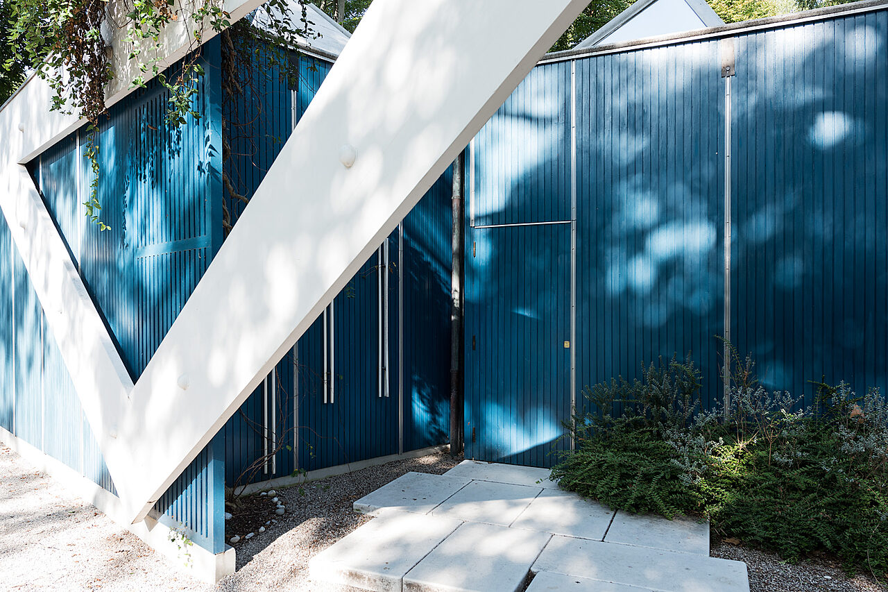 Aurinko heijastuu puiden takaa sinivalkoiseen Suomi-paviljonkiin.