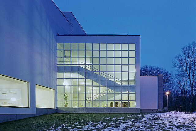 Viipurin kirjaston julkisivu, hämärtyvässä illassa. Julkisivun suuri ruutuikkunallisen seinän takana loistaa valaistu portaikko.