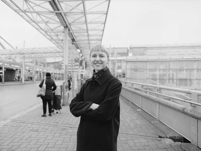 A woman standing under a bus canopy, gazing at the camera