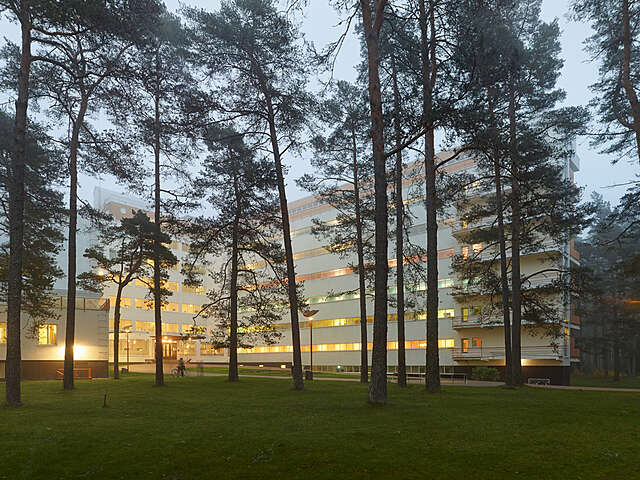 Paimion parantola iltahämärässä. Parantolan valot hohtavat pienen männikön takaa.