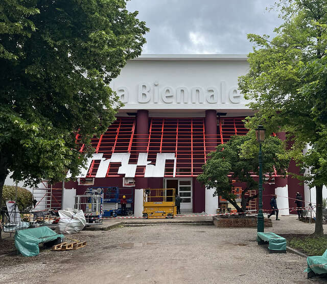 Rakenteilla oleva katosinstallaatio, taustalla rakennus, jossa lukee La Biennale