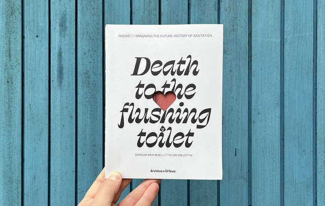 The picture shows the book "Death to the flushing toilet". There is a blue wooden wall in the background.
