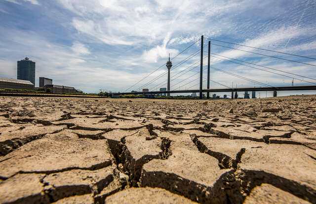A Dry river with a bridge standing on top of it and tall buildings in the background.