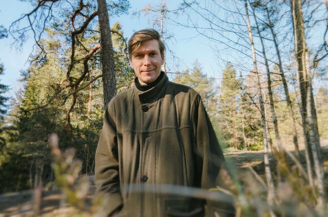 Nuorehko mies seisoo luonnossa yllään metsänvihreä takki