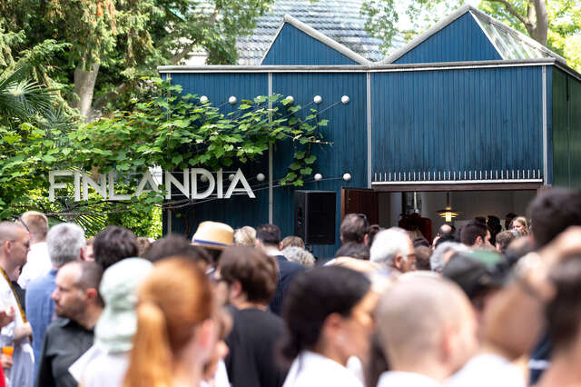 A crowd in front of a blue wooden pavilion with text Finlandia.