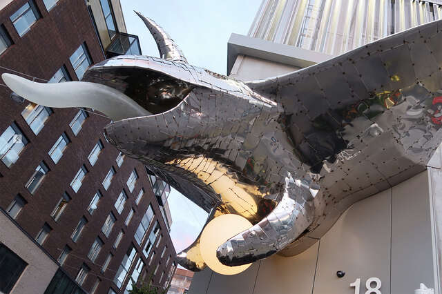 On the outside corner of the house, a lizard-like metal sculpture with a long tongue and a circular lamp between its paws.