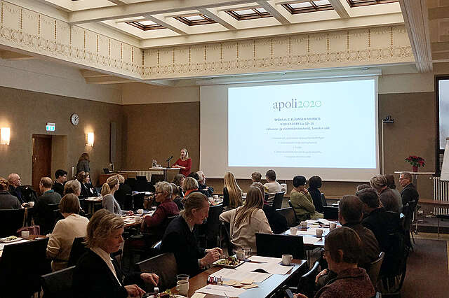 Sali, ihmisiä pöytien ääressä.