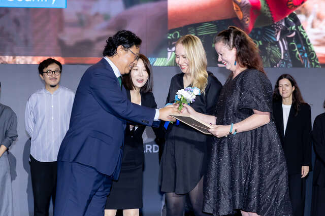 Aasialaisen näköinen mies ojentaa kukkia kahdelle naiselle