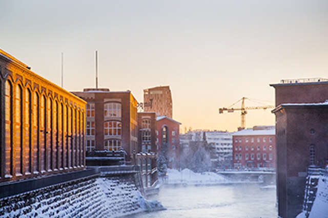 Punatiilisiä rakennuksia kosken molemmin puolin. Kosken rannoilla on lunta. Taustalla kohoaa huomattavan korkea kerrostalo sekä nostokurki.