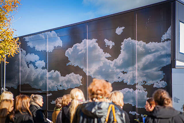 Kuva seinämaalauksesta, jossa on pilviä. Seinämaalauksen edessä seisoo useita ihmisiä.