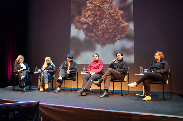 Kuusi ihmistä istuu esiintymislavalla