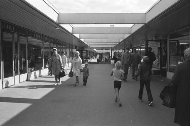 B&W photo of a pedestrian street aligned by low commercial buildings