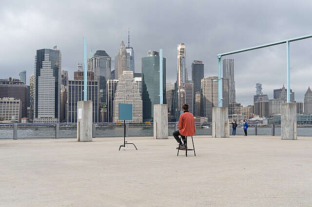 Punapaitainen mies istuu kentällä, taustalla näkyy Manhattanin pilenpiirtäjät.