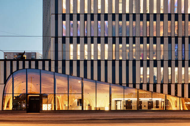 A close-up photo of a curved glass wall with an entrance, evening light.