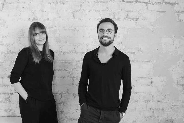Two people in front of a tile wall.