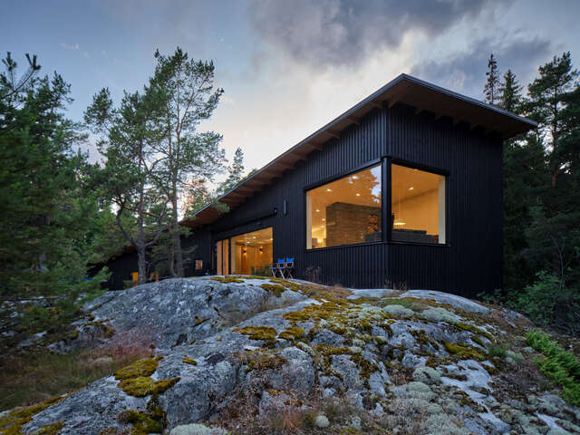 wooden building painted in black in a forest beside a cliff