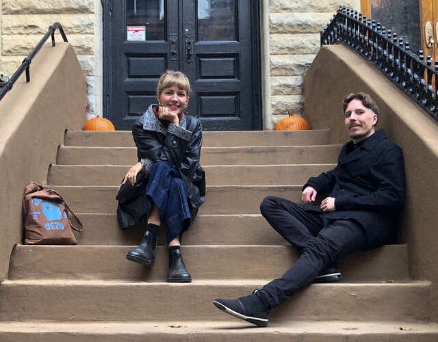 Two people are sitting on stairs and looking into the camera.