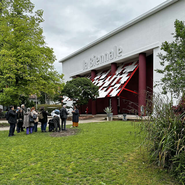 Group of people photographing a lady in front of a white building with an red and white installation and the word La Biennale