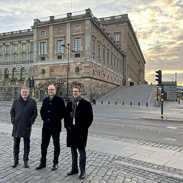Three men standing on the street, in front of a castle building