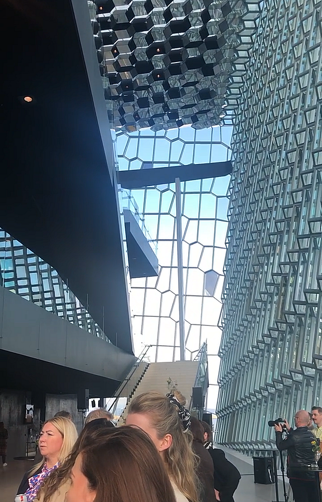 People in a high space surrounded by glass walls partitioned by a honeycomb-like structure